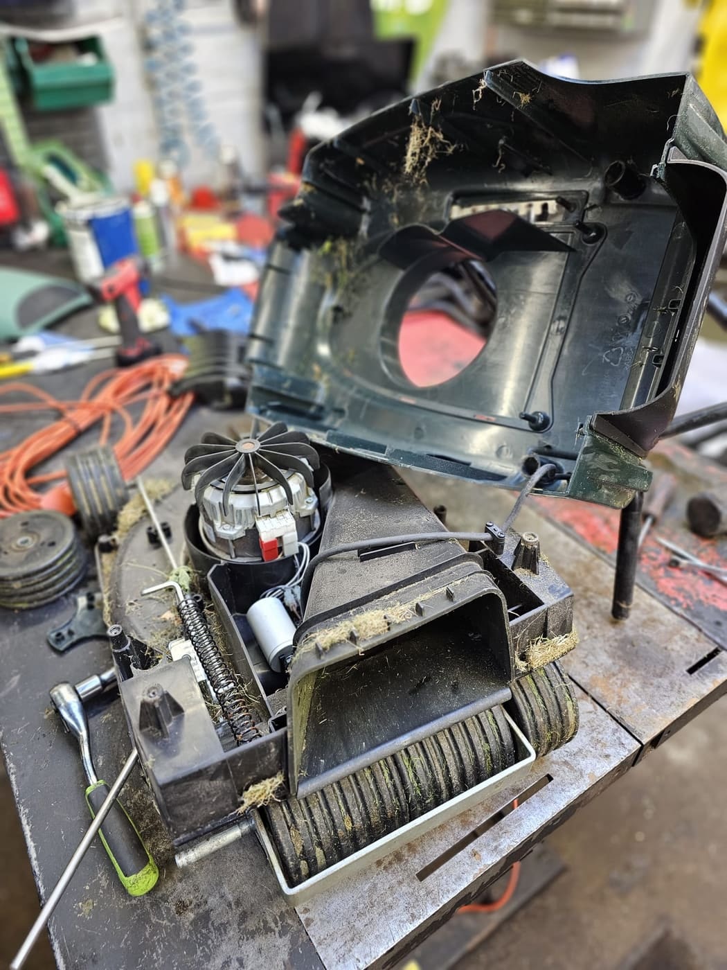 A Hayter Envoy stripped down on the workshop bench with grass packed in the chute