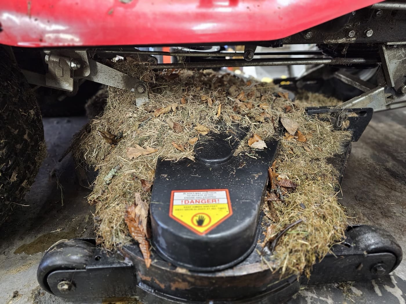 The cutting deck of a ride-on mower packed with grass and leaves