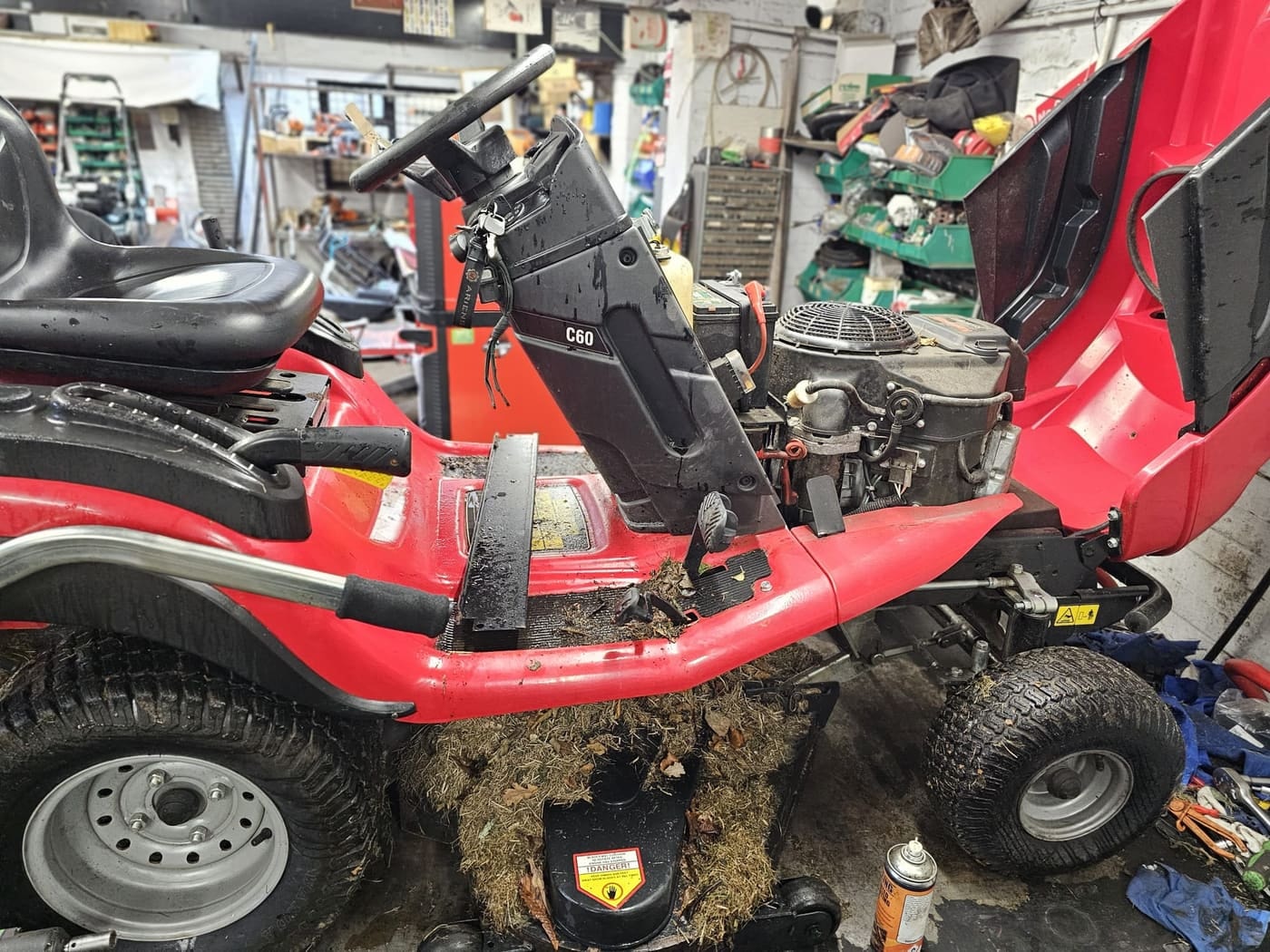 A ride-on mower with its bonnet up and grass packed under the deck