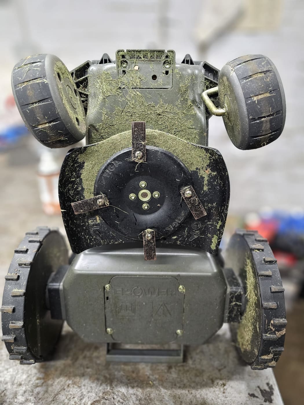 The grass-caked blade disc on the underside of a robot mower